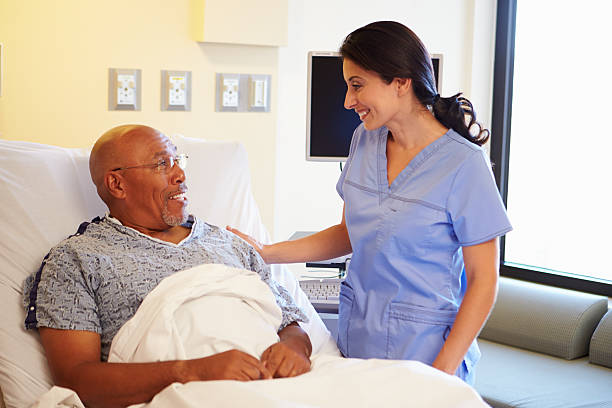 A smiling registered nurse talks to a patient lying in a hospital bed.
