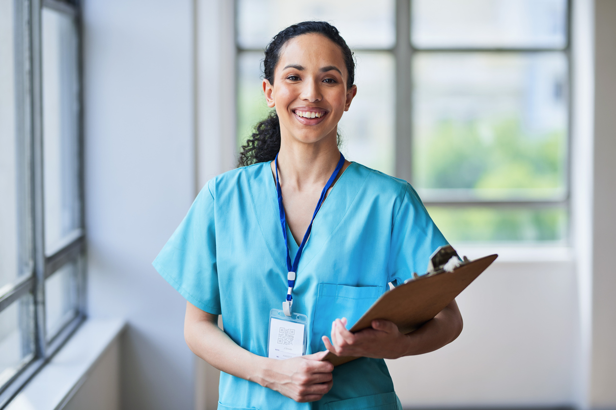 Smiling Nurse in Scrubs Holding a Clipboard in a Hospital Corridor.