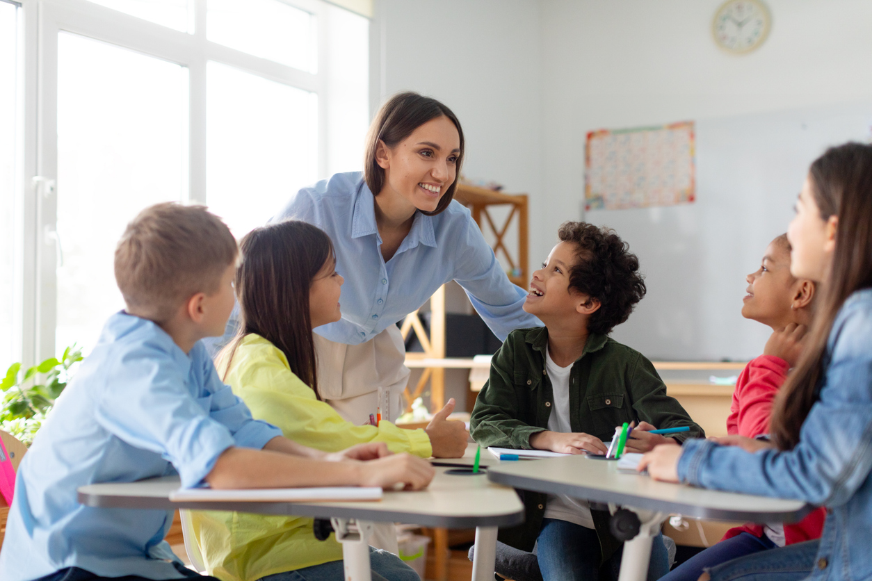 A Smiling Teacher Talks to a Group of Students in Class.