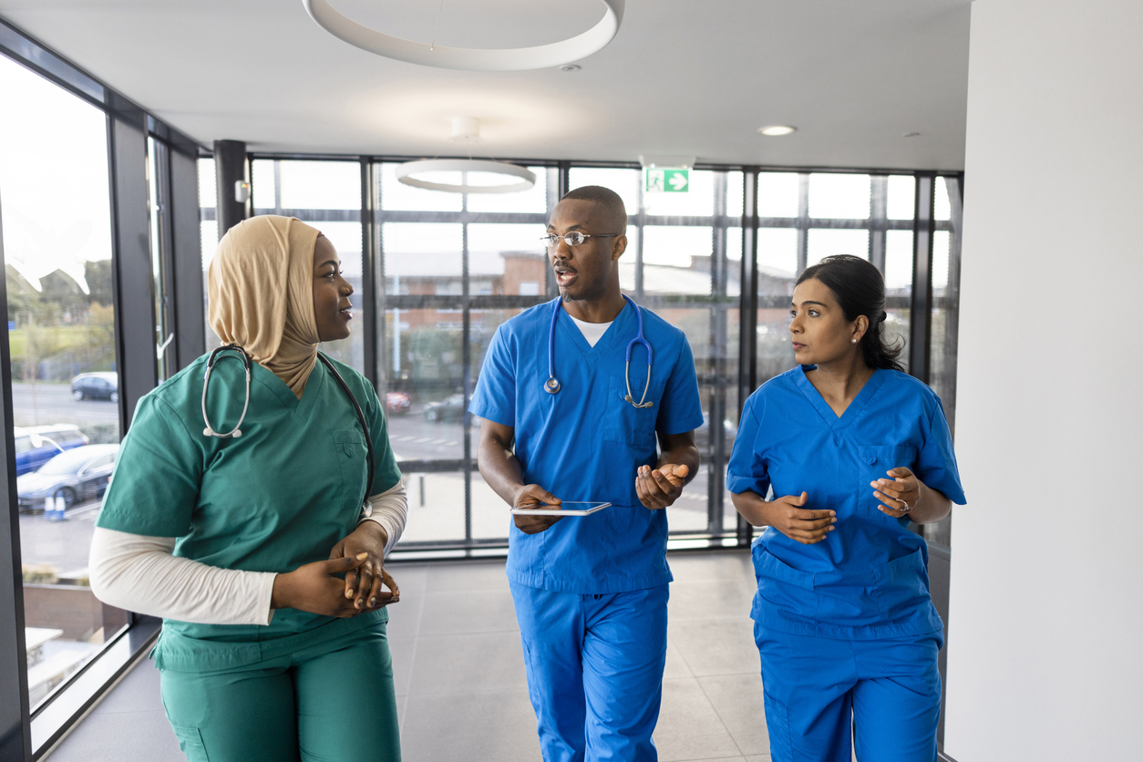 Three Nurses Talking as They Walk Down a Hospital Corridor.