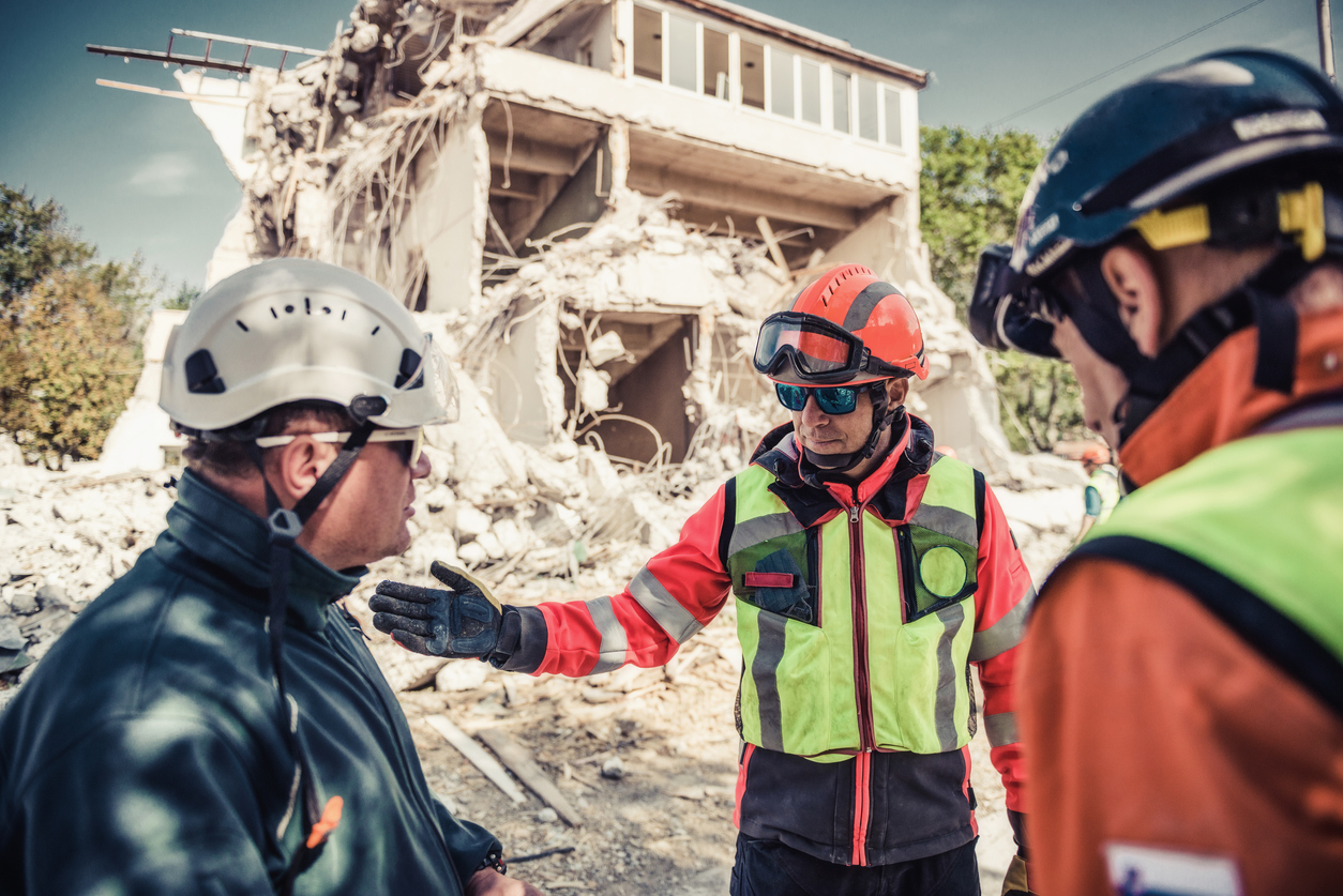 An emergency management director meets with an emergency response team in front of a damaged building.
